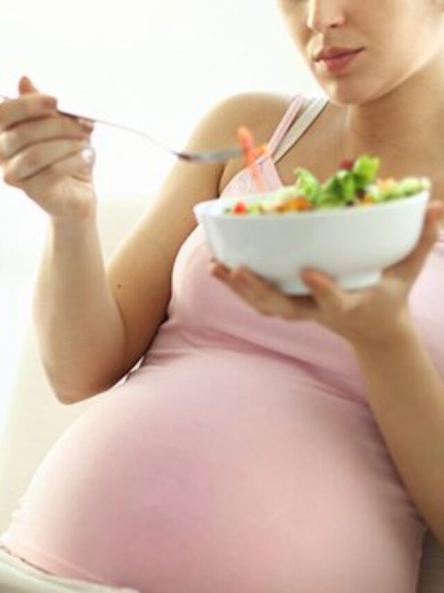 Pregnant woman relaxing at home and eating salad.